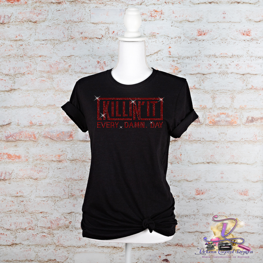 The black t-shirt from My Store, titled "Killin it," exudes bold style as it is displayed on a mannequin against a brick wall. The design features red text with a thin border that reads "KILLIN IT EVERY DAMN DAY." The shirt is stylishly knotted at the bottom, and a logo can be seen in the bottom right corner.
